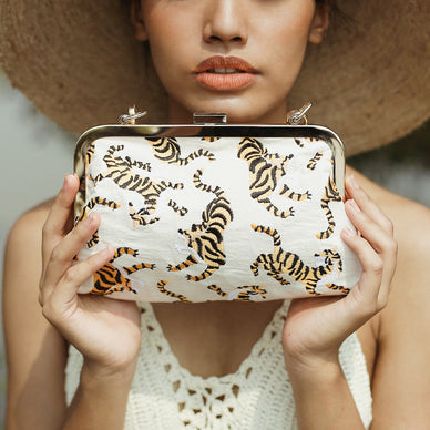 This clutch is our exclusive collection to shine the light to Indonesia's Sumatran tiger, one of the world's critically endangered animals. According to WWF, there are only fewer than 400 Sumatran tigers left and if deforestation poaching action continues, Sumatran tiger could be the first large predator to go extinct in the 21st century. 
Indonesia already has lost two tiger subspecies, the Bali and Javan tigers, which became extinct in the 1940s and 1980s respectively. Three of the world's eight tiger subspecies have gone extinct in the past 70 years; the remaining five subspecies are all endangered. 

WWF supports anti-poaching patrols in Indonesia and has helped arrest and prosecute poachers. WWF is also investing in habitat conservation and a biological assessment of tigers in the lowlands of central Sumatra to better address threats to the remaining population. 
How we can help: Share this story, switch to sustainable products to protect our forests, donate to organizations that support anti-poaching actions to protect Sumatran tigers. Take action here: 
International Tiger Project https://www.internationaltigerproject.org/donate/ 
WWF Indonesia - Sahabat Harimau https://www.wwf.or.id/cara_anda_membantu/bertindak_sekarang_juga/sahabatharimau/ 
Fauna Flora International https://www.fauna-flora.org/species/sumatran-tiger 
We hope through this Sumatran tiger clutch, we can help share the story to raise awareness to this critical condition, and inspire people to take action. 
Sumatran Tiger Clutch detail: • Dimension: 8.75" W x 6.2 H x 2.75 D • Strap drop: 11.75 inches • Composition: Handwoven Raw Cotton fabric, Cotton Embroidery, Gold metal chain strap 
*** We will donate the proceeds from each Sumatran tiger clutch purchased directly from our website to one of the organizations listed above. 
Ships separately from our friends at BrunnaCo 